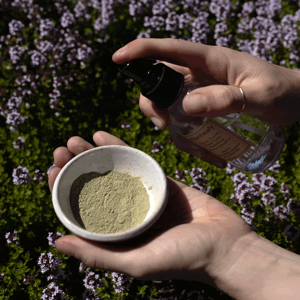 Hands hold Green Tea Clay Mask powder in a bowl while misting it with a spray bottle outdoors