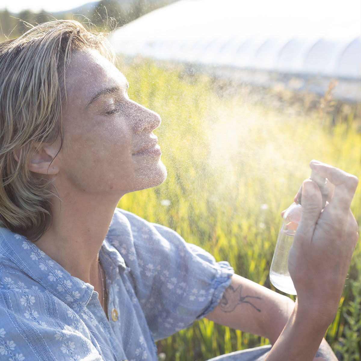 Woman sprays hydrosol mist on her face outdoors in a sunlit field