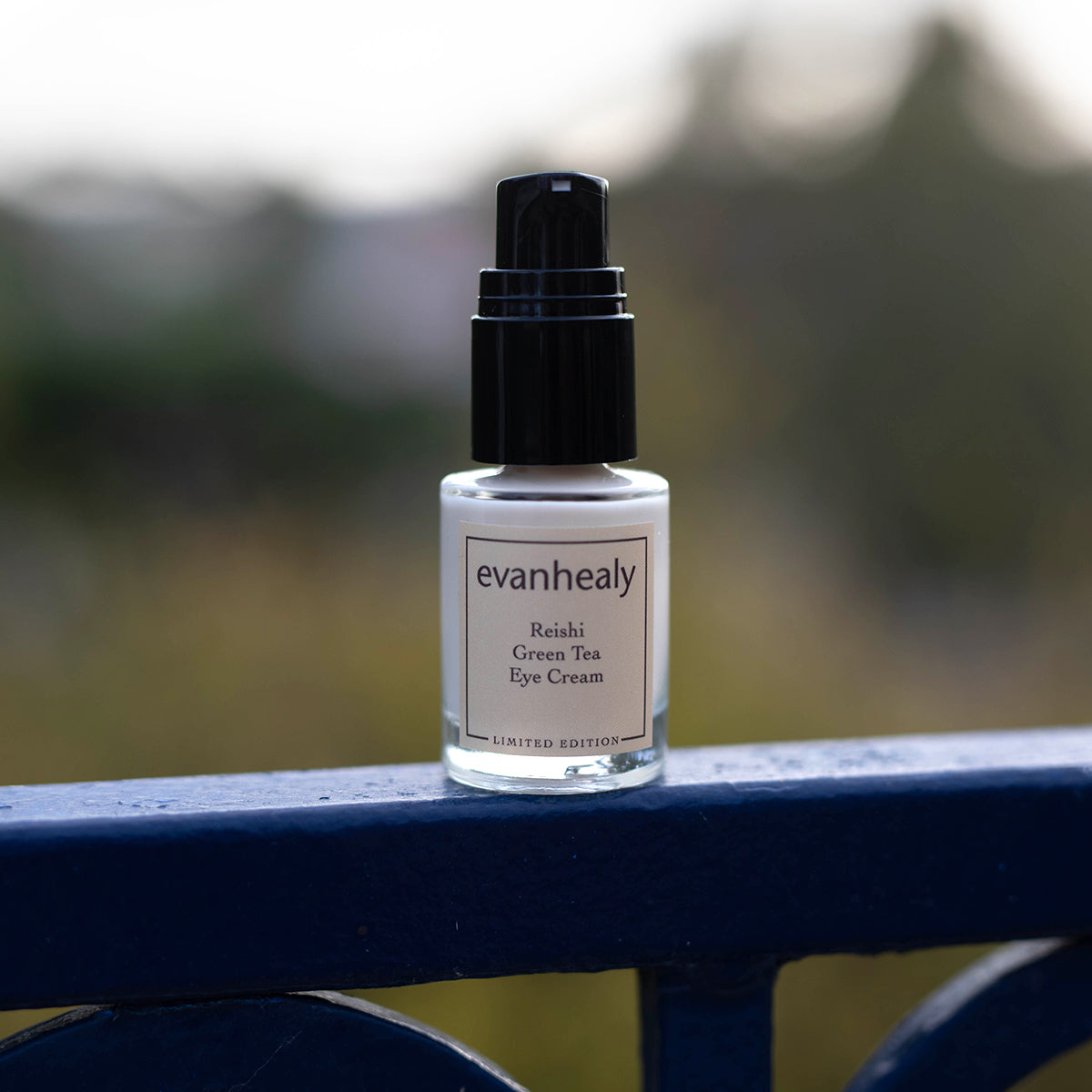 Close-up view of evanhealy Reishi Green Tea Eye Cream bottle showcasing its black pump with blurred outdoor background
