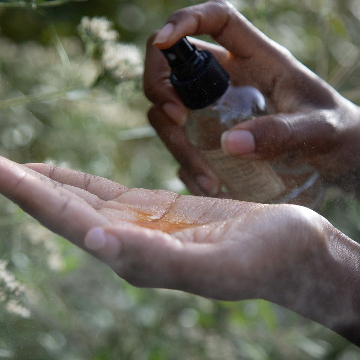 Hands dispensing Pomegranate Vitality Serum into a palm outdoors