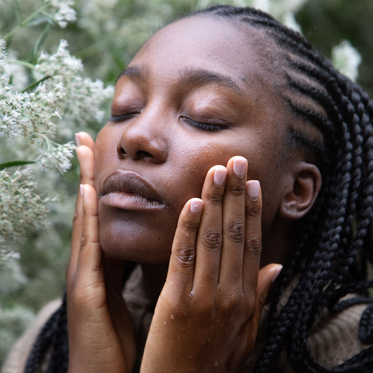 Woman massaging her face outdoors among greenery