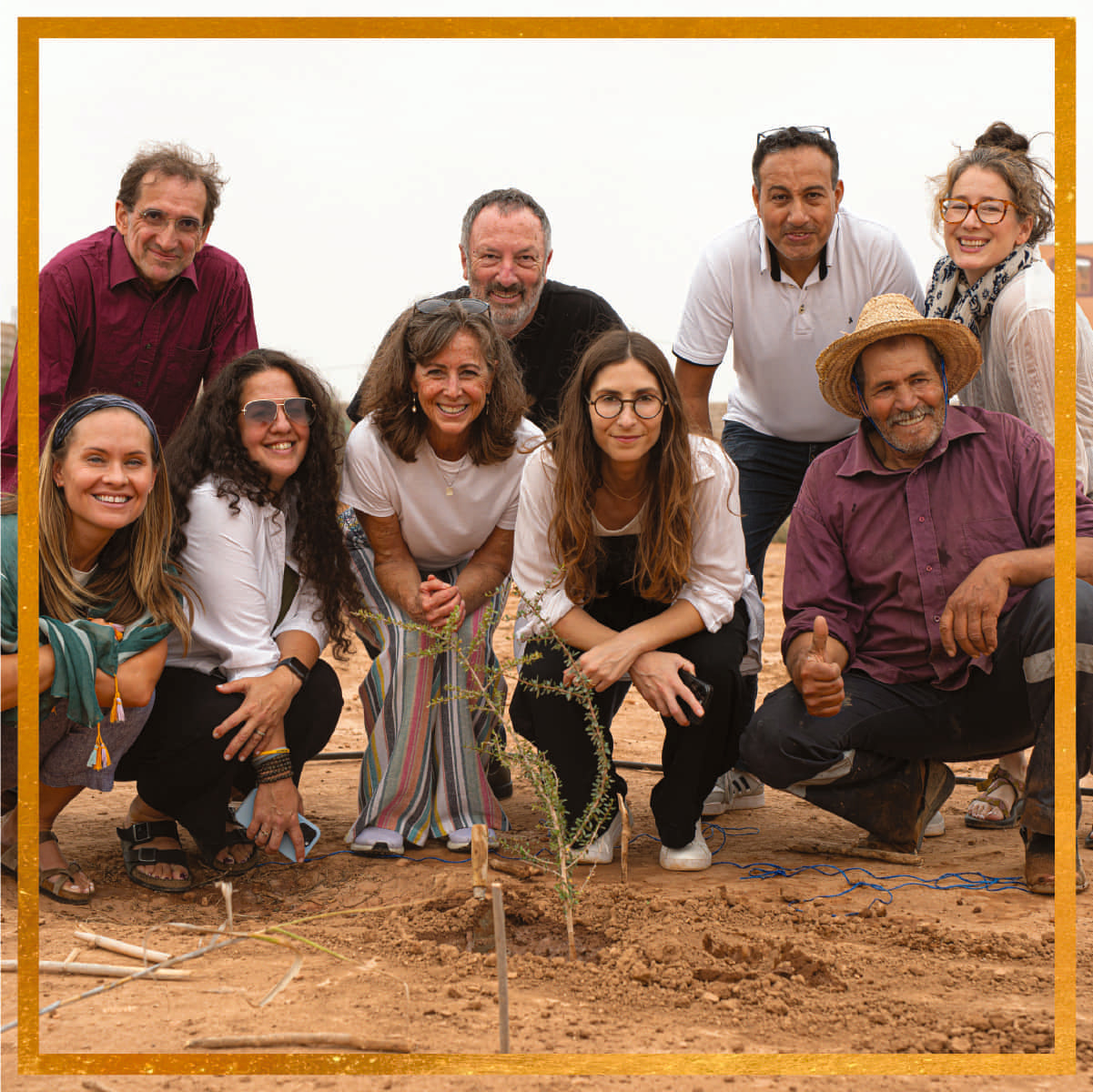 Group of Al‑Amal cooperative members and partners planting a young argan tree in Tiznit, Morocco, smiling at the camera