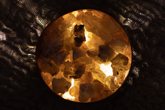Top-down view of frankincense resin in a bowl showcasing amber pieces lit from within against a dark textured background