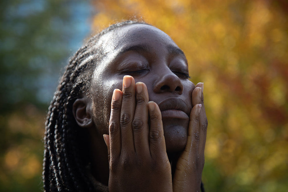 Woman gently pressing her hands to her face during a skincare ritual outdoors