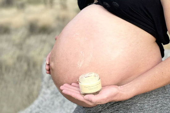 Pregnant woman holding a jar of Whipped Shea Butter with Olive Leaf on her bare baby bump outdoors