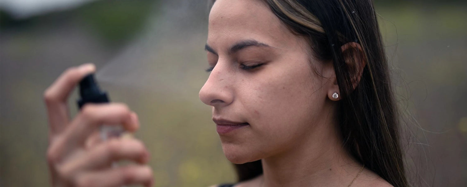 Woman with acne-prone skin closing her eyes while a facial mist is sprayed outdoors