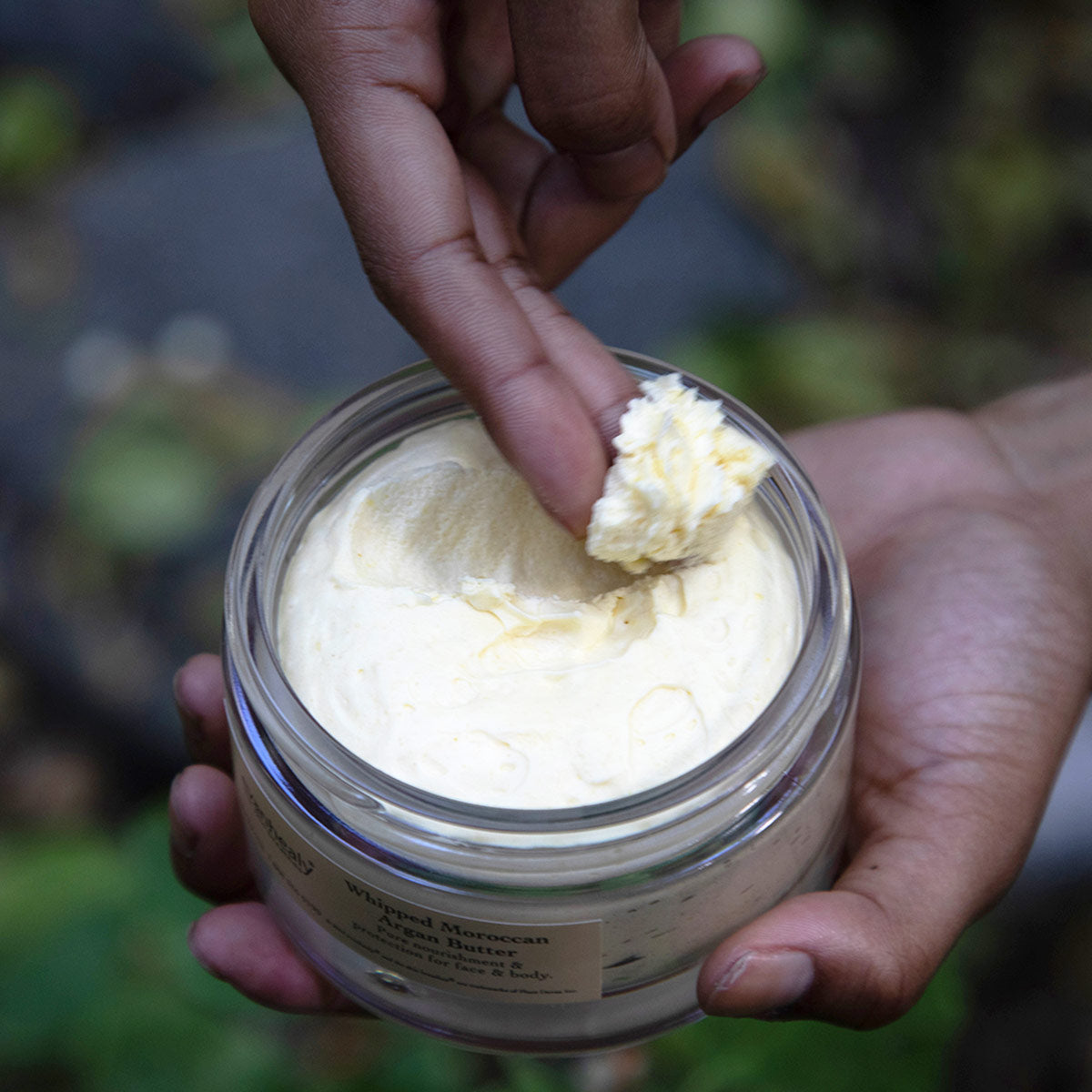 Close-up of Whipped Moroccan Argan Butter showcasing its whipped texture with hands holding the open jar in nature
