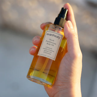 Close-up of Neroli Frankincense Body Oil in a pump bottle held in a hand against a softly blurred background