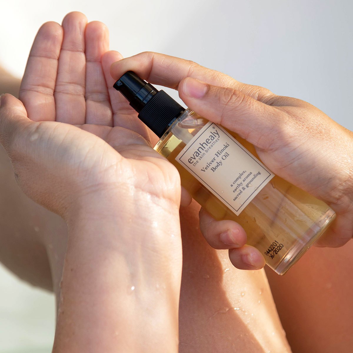 moisturizing body oil being pumped into hand in bath tub to moisturize skin