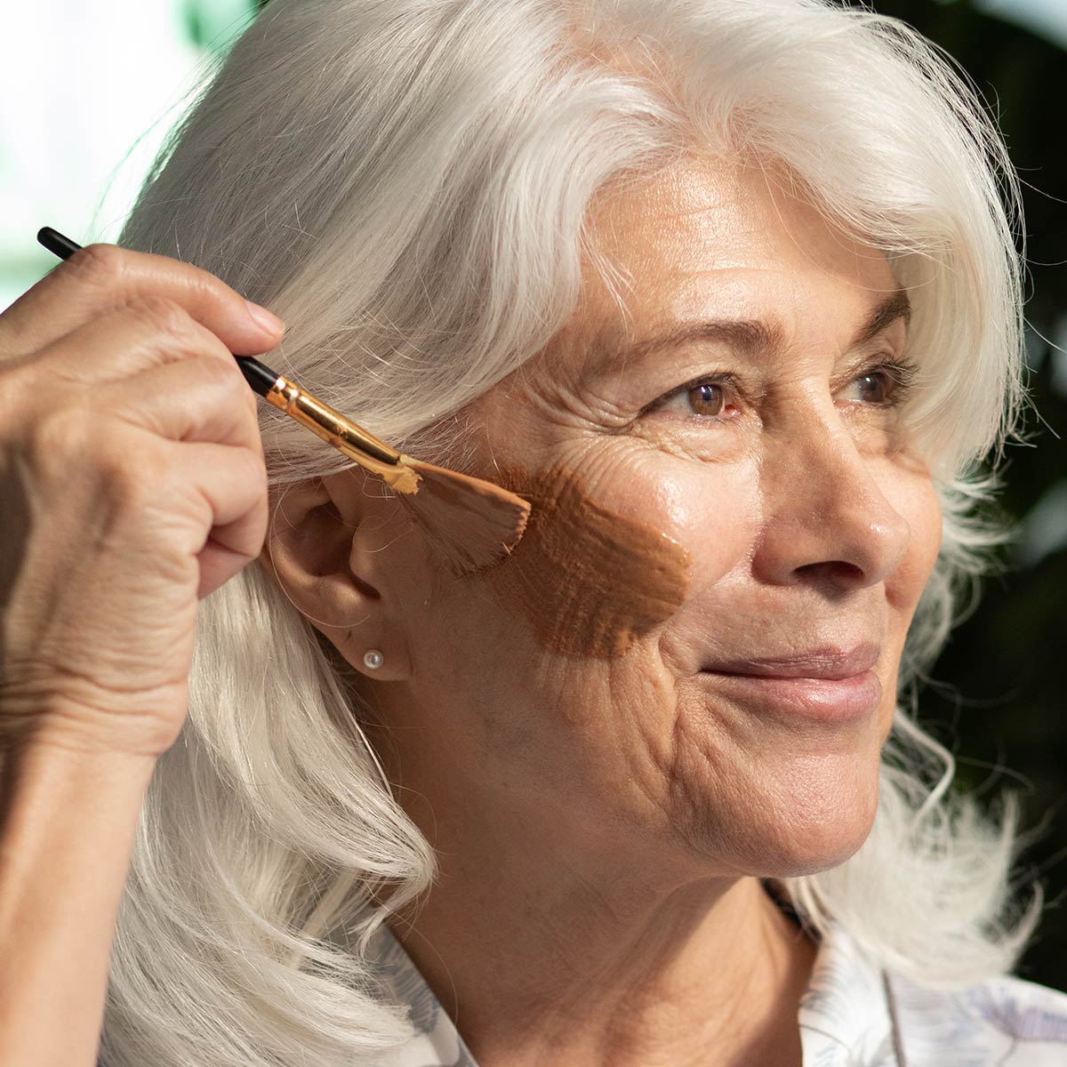 model applying french rose clay mask to face with natural boars hair brush