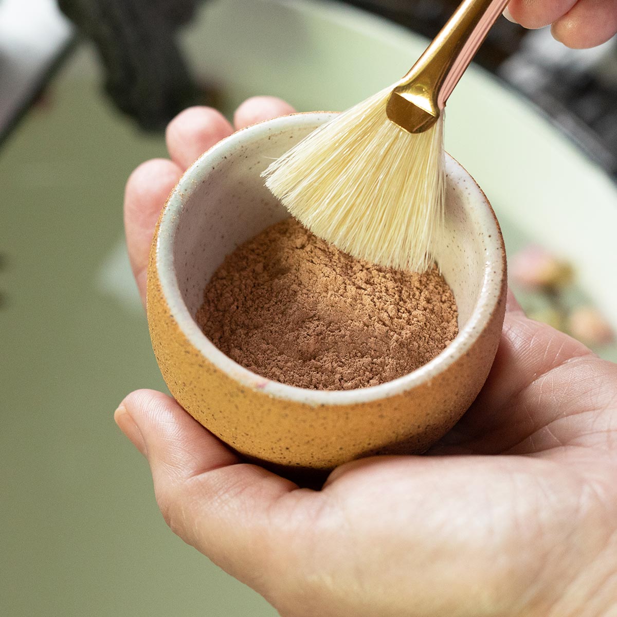 Hands hold a ceramic bowl of French Rose Clay Mask powder beneath a facial brush