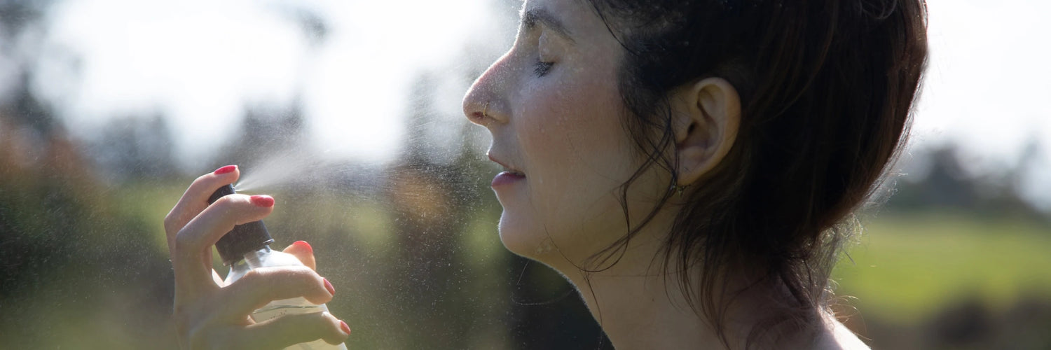 Woman spraying a hydrating facial mist onto her face outdoors in sunlight