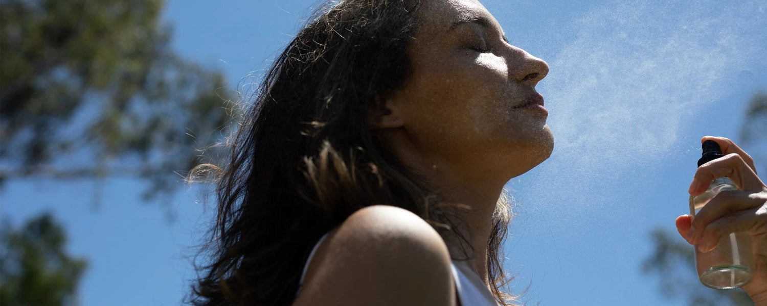 Woman spraying facial mist outdoors against a clear blue sky
