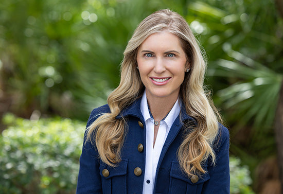 Andrea Larsen smiling portrait in a leafy outdoor garden, wearing a navy jacket and white blouse