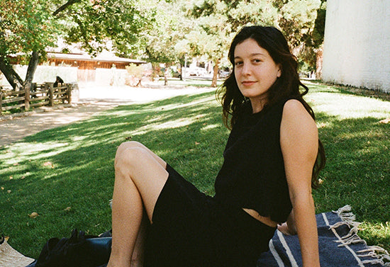 Woman seated on a blanket on grass in a sunny park, smiling at the camera