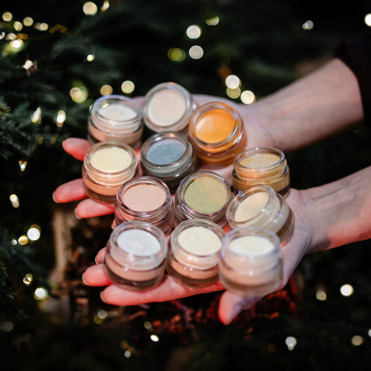 Close-up of Twelve Days of Christmas skincare collection showcasing multiple jars in hands with a Christmas tree background