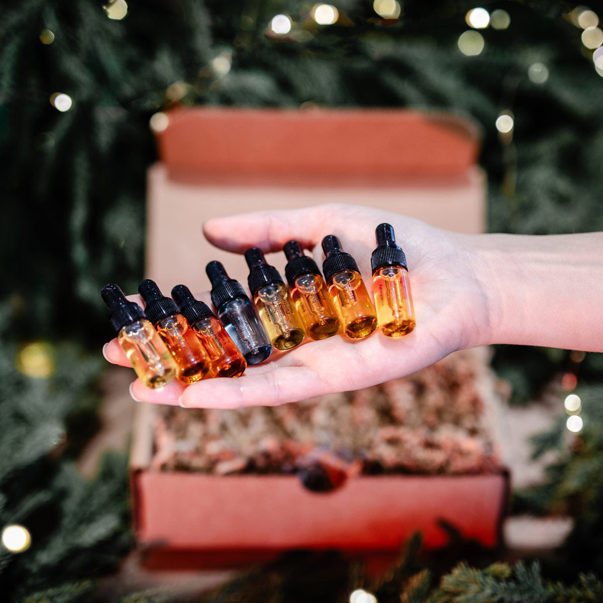 Close-up of Eight Nights of Oil bundle showcasing eight oil bottles in a hand with a festive gift box background
