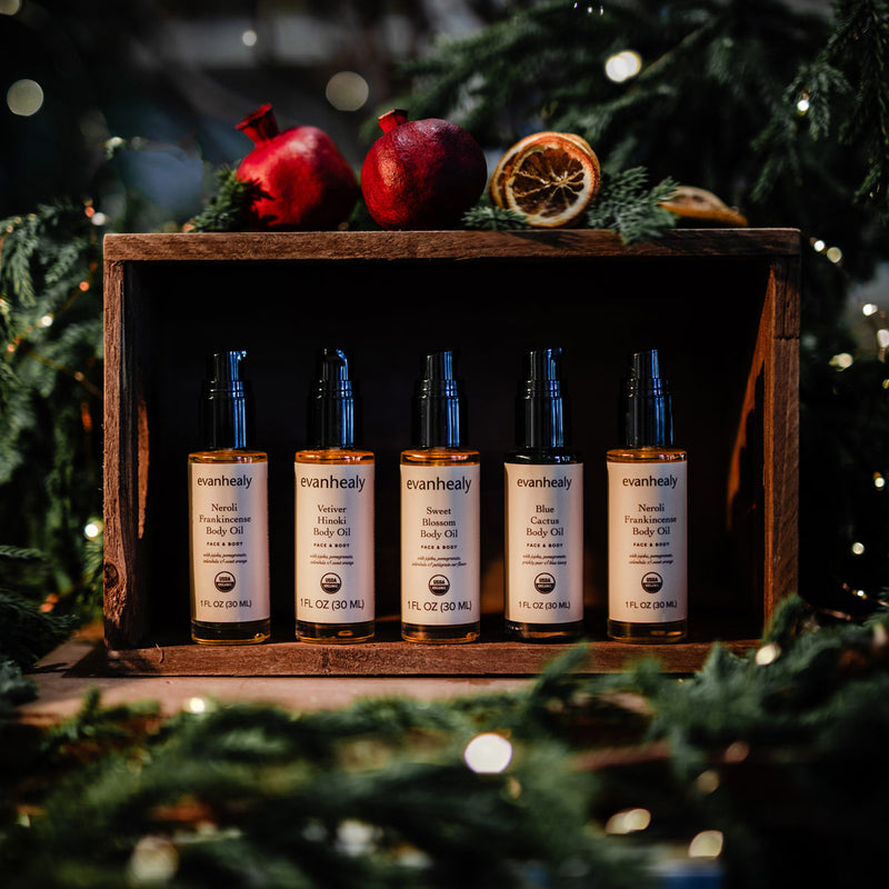 Front view of Body Oil Flight showcasing five 2 ounce body oil bottles in a wooden gift box with evergreen branches