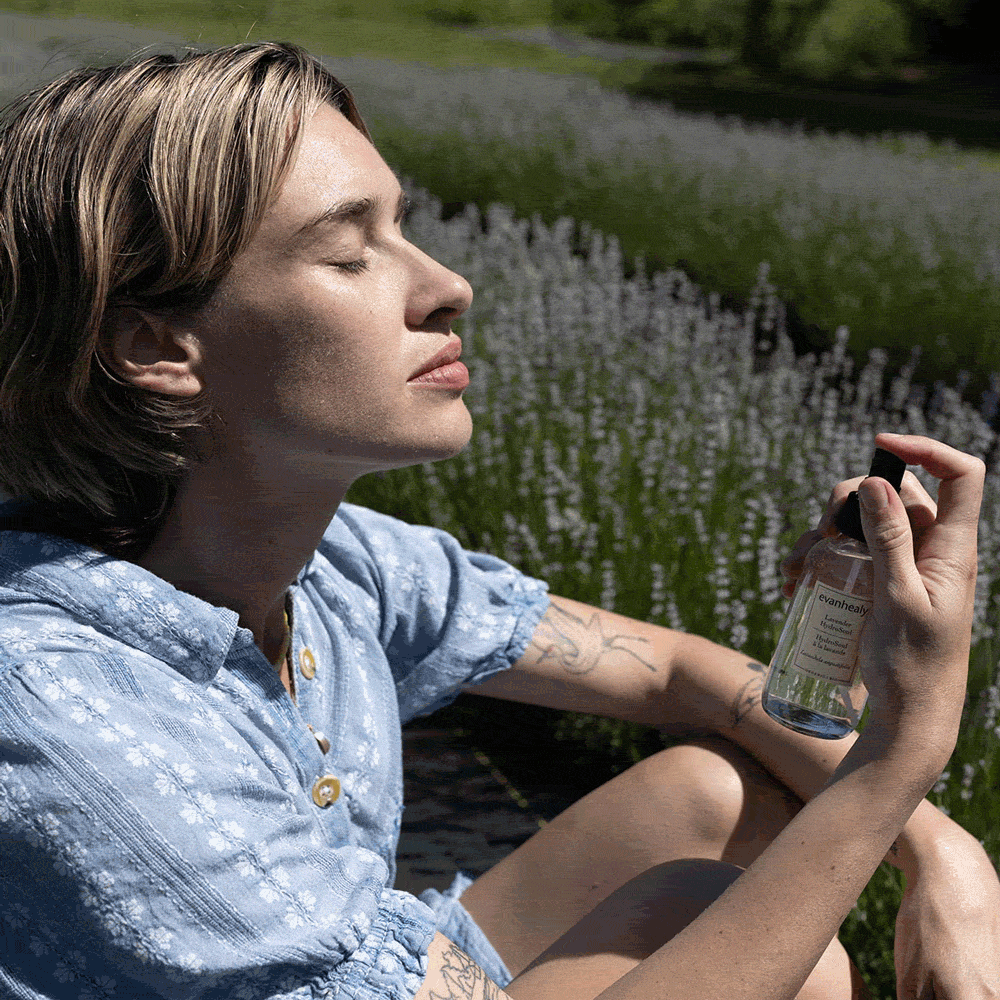 Woman spraying Lavender HydroSoul facial toner while sitting in a lavender field