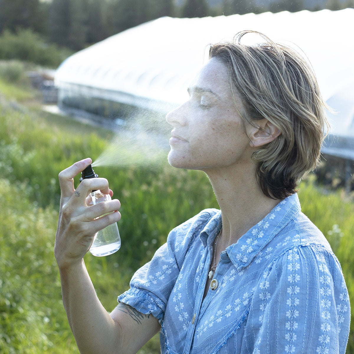Woman spraying Sweetgrass Hydrosol outdoors in a sunny field