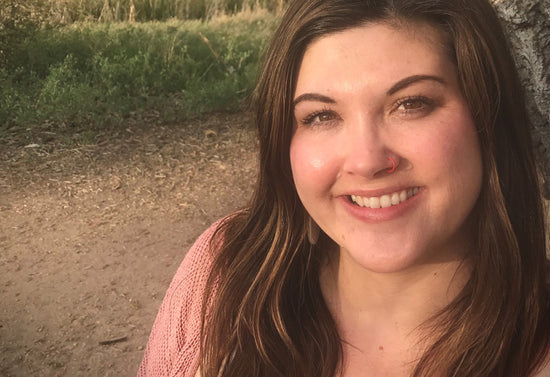 Esthetician Laura Jensen smiling in an outdoor portrait with trees and a dirt path behind her