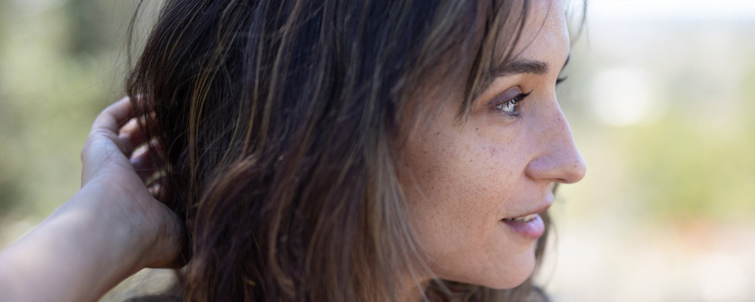 Woman in profile touching her hair outdoors, showing mature skin in soft natural light