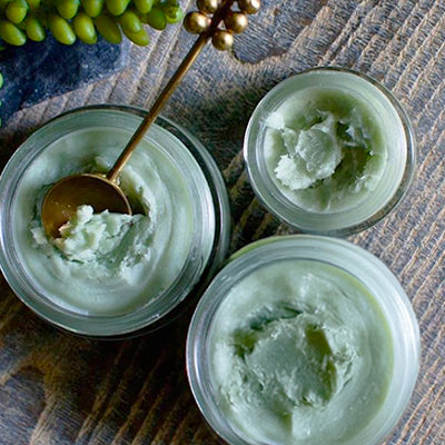 Top view of Blue Cactus Beauty Balm showing pale green balm texture in glass jars with a spoon on rustic wood