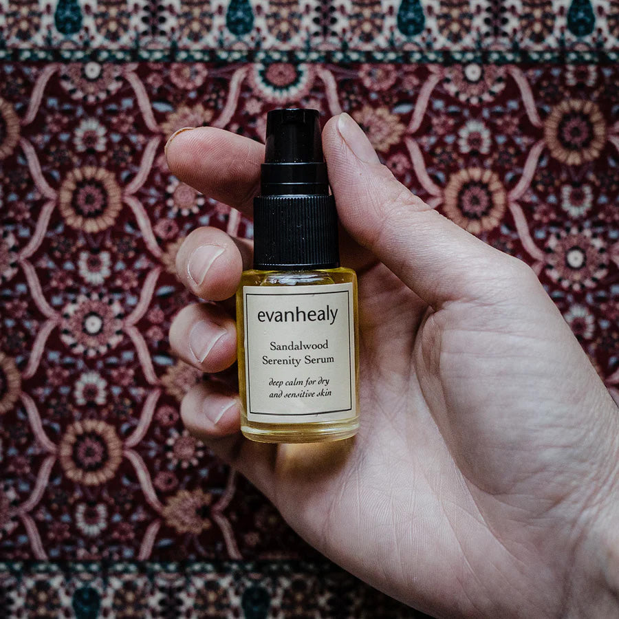 Front view of Sandalwood Serenity Serum showcasing its black pump and labeled glass bottle held against patterned fabric