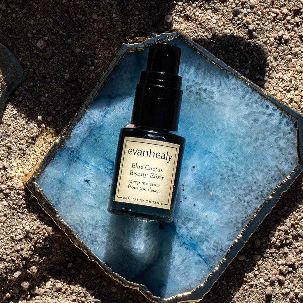 Top-down view of Blue Cactus Beauty Elixir showcasing its pump bottle on a blue stone surrounded by sand