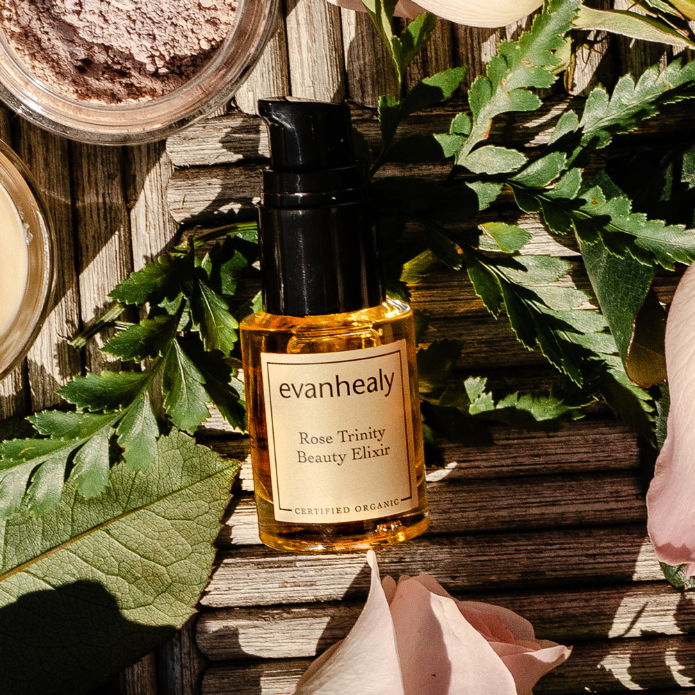 Front view of Rose Trinity Beauty Elixir facial oil serum in an amber dropper bottle with botanical leaves and rose petals