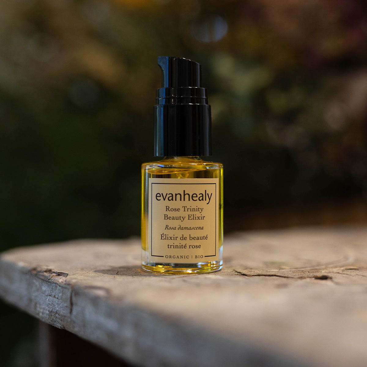 Front view of Rose Trinity Beauty Elixir facial oil serum showcasing its amber bottle and pump on a weathered stone surface