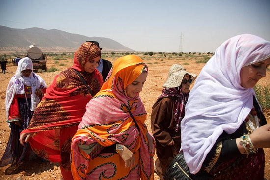 Women from the Al‑Amal cooperative walking across an arid Moroccan landscape wearing colorful headscarves