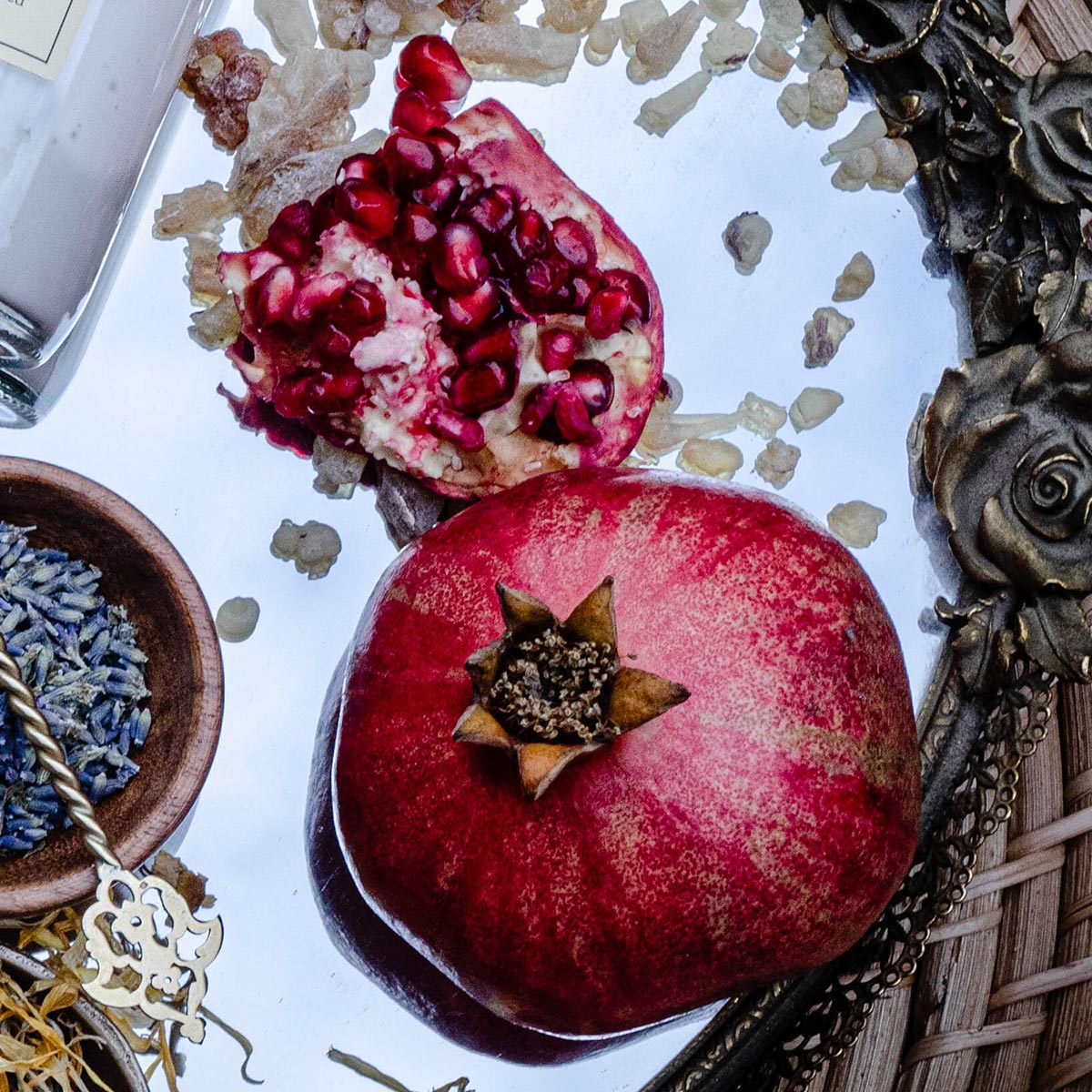 Pomegranate fruit and seeds arranged with dried botanicals on a reflective surface