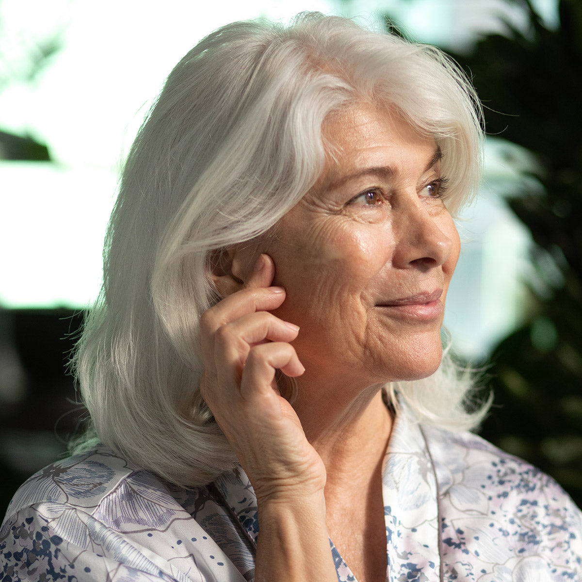 Older woman applying Sea Algae Serum to her face in a bright natural setting