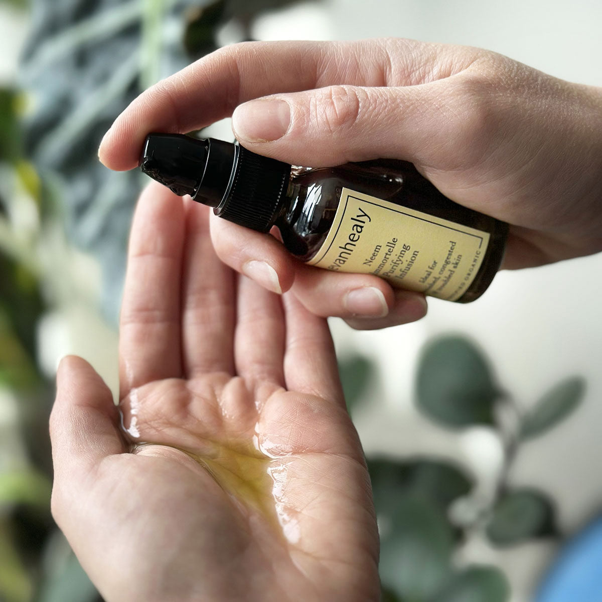 Close-up view of Neem Immortelle Purifying Infusion bottle showcasing oil in an open palm with blurred greenery
