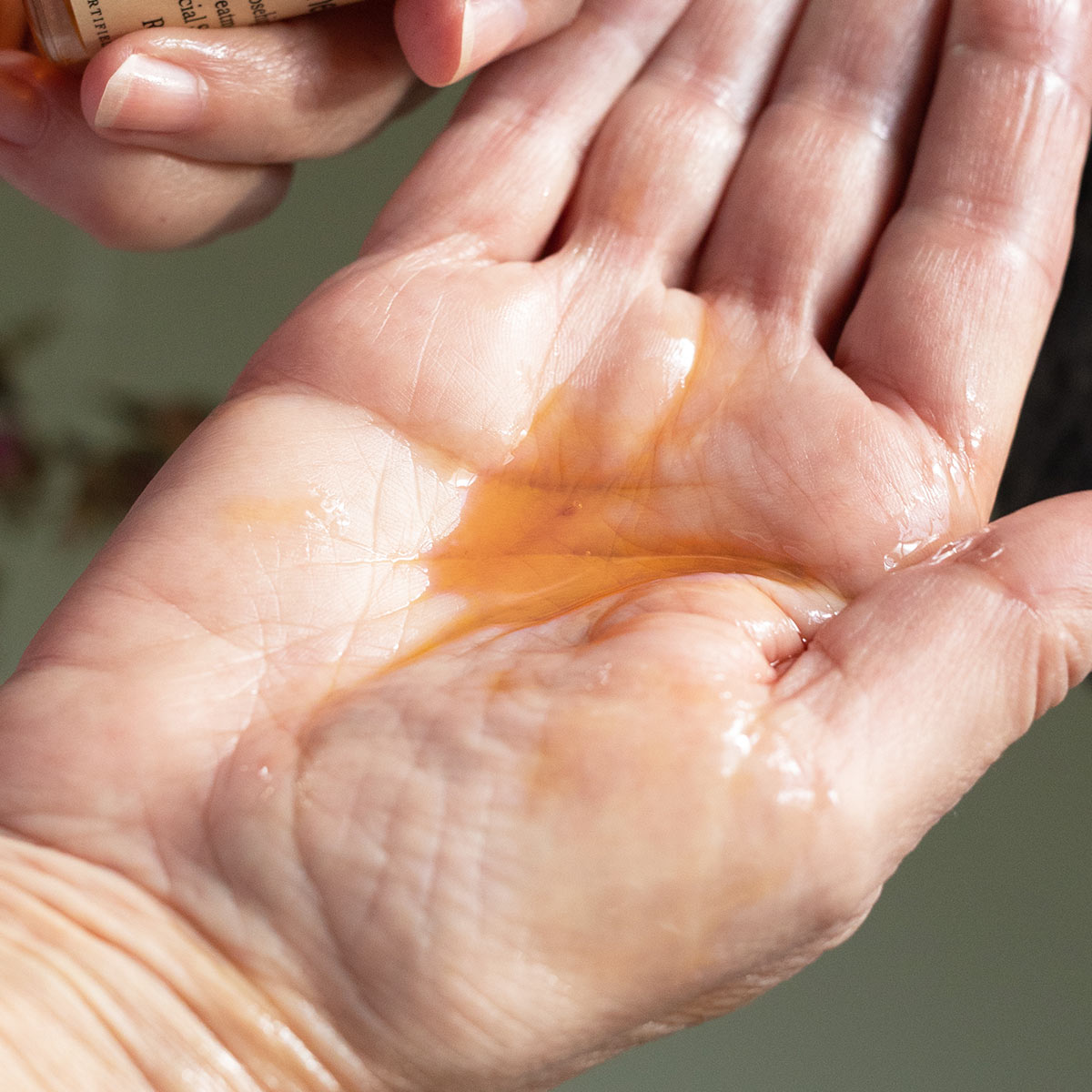 Close-up of Rosehip Calming Serum dispensing amber oil into palm, showing lightweight glossy texture with soft green background