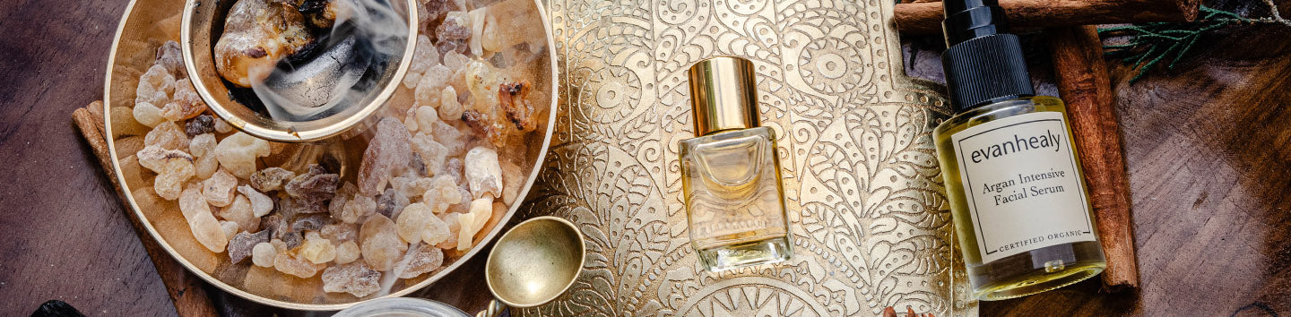 Evanhealy serum bottle and small perfume bottle beside a bowl of frankincense resin on an engraved brass tray with cinnamon sticks