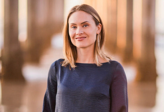 Esthetician smiling for a portrait outdoors with warm, blurred architectural columns in the background