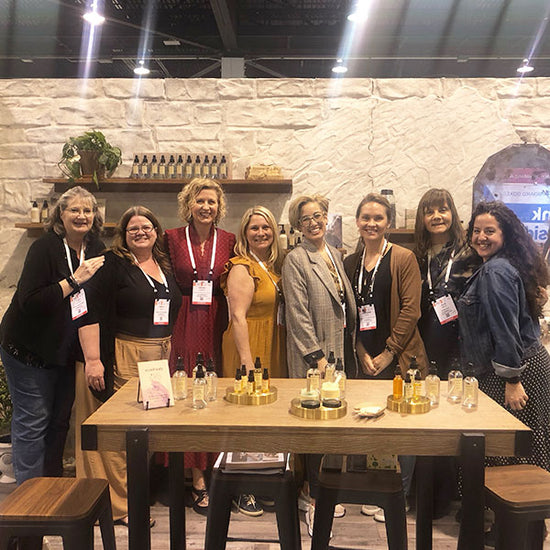Group of staff posing behind a booth table with skincare bottles and jars on display at a trade show
