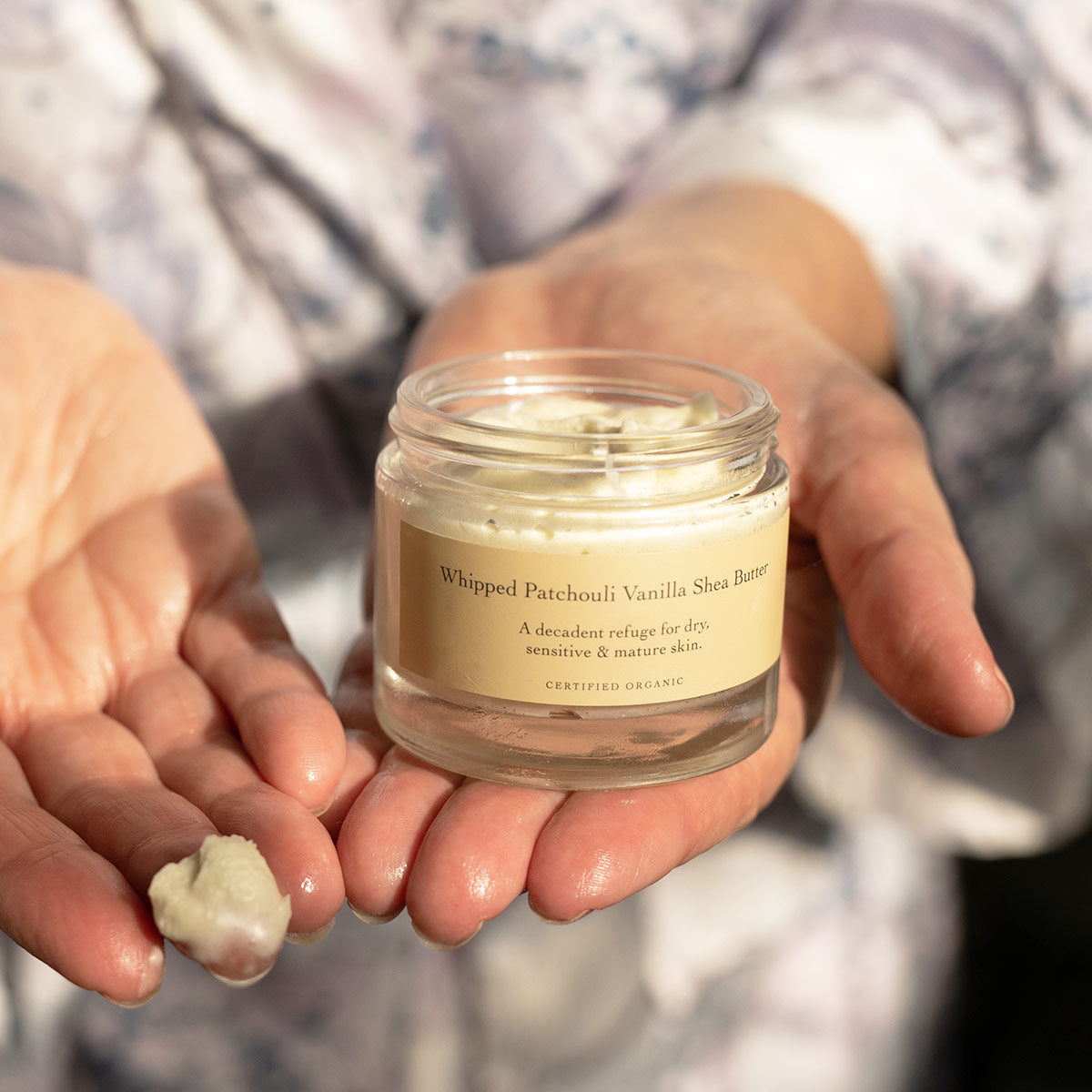 Close up of Whipped Patchouli Vanilla Shea Butter showcasing whipped shea butter in an open glass jar held in hands